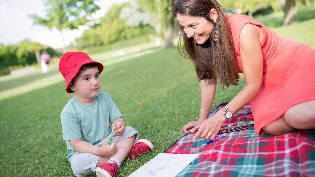 A happy moment between a mother and child drawing outdoors on a picnic blanket.